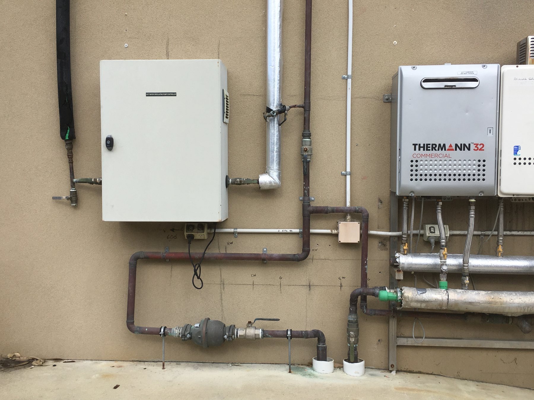 Twin commercial gas water heaters mounted with insulated flow and return pipework.