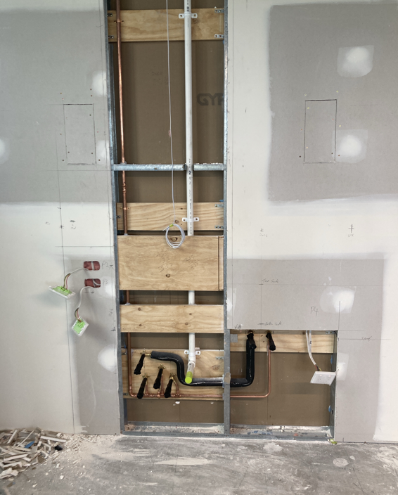 Copper and PVC rough-in set out on ply backing in a stud wall before lining.